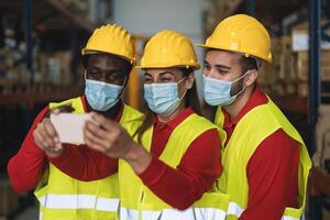 Multiracial teamwork having fun taking selfie while working in warehouse wearing face mask during corona virus outbreak - Logistic and industrial concept photo