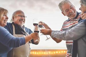 Happy seniors friends drinking red wine on terrace sunset - Mature people having fun laughing and sharing time together outdoor - Elderly retirement lifestyle activity  concept photo