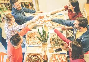 grupo de amigos tostado lentes de cerveza mientras comiendo Pizza en su casa - contento personas disfrutando cena juntos con sabroso tomar lejos comida a hogar - concepto de amistad, compañía, estilo de vida foto