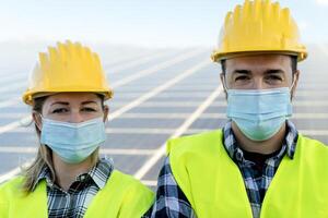 People working for alternative energy with wind turbine and solar panel while wearing face mask during corona virus outbreak - Innovation and green power concept photo