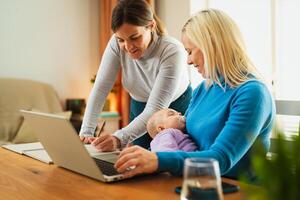 Happy lesbian couple working on laptop while their small baby is sleeping - LGBT family and technology concept photo