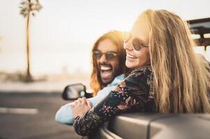 Happy young couple doing road trip in tropical city - Travel people having fun driving in trendy convertible car discovering new places - Relationship and youth vacation lifestyle concept photo