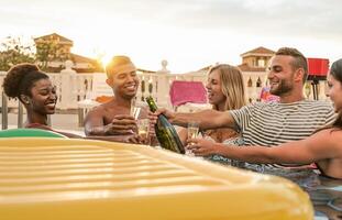 Group happy friends making a pool party cheering with champagne at sunset - Young people laughing and having fun toasting with sparkling wine in luxury tropical resort - Youth lifestyle concept photo