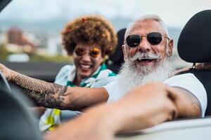 Happy senior couple having fun driving on new convertible car - Mature people enjoying time together during road trip tour vacation - Elderly lifestyle and travel culture concept photo