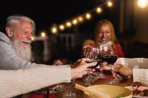 Happy multiracial seniors toasting with red wine glasses and celebrating holidays on house patio dinner - Elderly lifestyle people concept photo