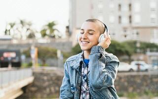 Shaved head girl listening to music with wireless headphones in the city street photo