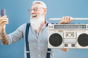 mayor loco hombre utilizando teléfono mientras escuchando música con Clásico boombox - hipster chico teniendo divertido utilizando móvil teléfono inteligente lista de reproducción aplicaciones - personas felicidad y mayor tecnología fanático concepto foto