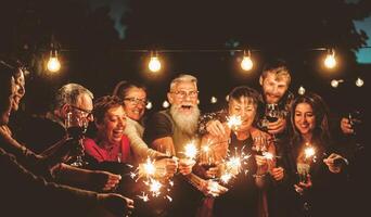 contento familia celebrando con bengalas fuegos artificiales a noche fiesta - grupo de personas con diferente siglos y etnia teniendo divertido juntos - Días festivos estilo de vida concepto foto