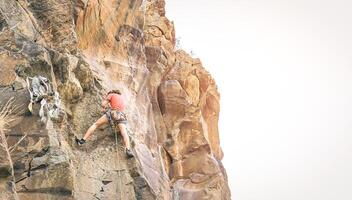 atlético hombre clambing un rock pared a puesta de sol - trepador ejecutando en un cañón montaña - concepto de deporte y extremo estilo de vida foto