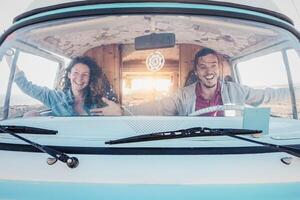 Happy travel couple having fun driving vintage minivan during road trip tour - Youth people vacations lifestyle concept photo