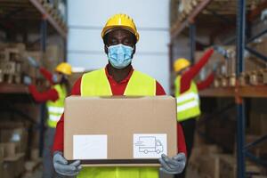 negro hombre trabajando en almacén cargando entrega cajas mientras vistiendo cara quirúrgico máscara durante corona virus pandemia - logístico y industria concepto foto