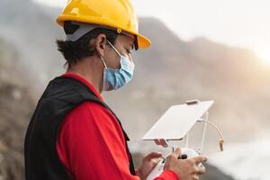 Male engineer monitoring the drone inspection while wearing face mask to avoid corona virus spreading - Technology and industrial concept photo