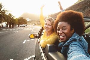 Young happy women taking selfie doing road trip - Travel girls having fun driving in trendy convertible car discovering new places - Friendship and youth girlfriends vacation lifestyle concept photo