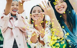 Happy Asian friends having fun throwing confetti outdoor - Young trendy people celebrating at festival event outside - Party, entertainment and youth holidays lifestyle concept photo