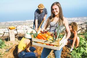 Group of friends working together in a farm house - Happy young woman holding fruit crate with fresh vegetables in the garden house - Agriculture, healthy food and vegetarian lifestyle concept photo