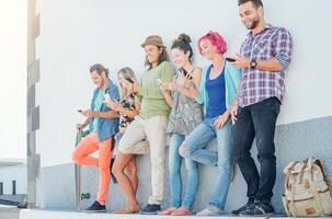 Young people watching on their smart mobile phones leaning on a wall - Generation addicted to new technology - Concept of youth addiction to social network trends photo