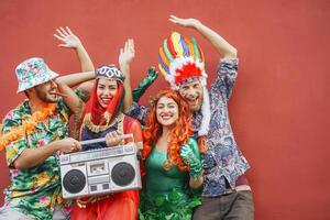 Happy friends celebrating carnival party outdoor - Young crazy people having fun wearing costumes listening music with vintage boombox stereo - Youth holidays culture lifestyle concept photo