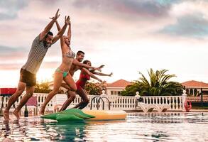 Group of happy friends jumping in pool at sunset time - Millennial young people having fun making party in exclusive resort tropical - Holidays, summer, vacation and youth lifestyle concept photo