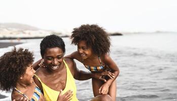 Happy African family playing on the beach during summer holidays - Afro American people having fun on vacation time - Parents love and travel lifestyle concept photo