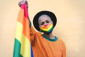 Young woman wearing gay pride mask holding rainbow flag symbol of Lgbtq social movement photo