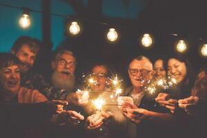 Happy family celebrating new year eve with sparkler outdoor - Group people with different ages and ethnicity having fun together in night party outside - Youth and elderly friendship lifestyle concept photo