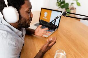 African man recording a podcast using microphone and laptop from his home studio photo