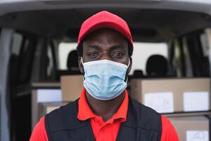 African delivery man working while wearing face mask to avoid corona virus spread - People working with fast deliver during corona virus outbreak photo