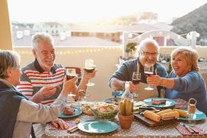 Happy senior friends dining and drinking red wine on house terrace - Mature people having fun laughing together at dinner party - Food and elderly friendship lifestyle concept photo