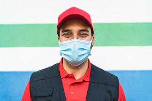 Delivery man wearing face protective mask to avoid corona virus spread - Young express courier working during coronavirus outbreak - Deliver and online buying concept photo