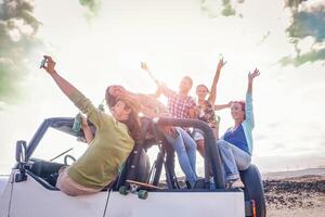 grupo de contento amigos teniendo divertido en convertible coche en vacaciones - joven personas Bebiendo champán y tomando selfie durante su la carretera viaje - viajar, amistad, juventud estilo de vida Días festivos concepto foto