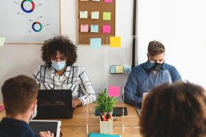 Young people in co-working creative space wearing surgical mask and keeping social distance to avoid corona virus spread - Health care and business technology concept photo