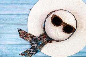 Top view of a straw white hat with glasses lying on a blue wooden background.Summer vacation concept photo