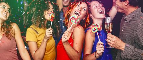 Happy friends celebrating new year eve drinking champagne in nightclub - Young people having fun dancing with lollipops in disco club - Youth culture entertainment lifestyle and nightlife concept photo