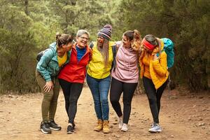 Happy women with different ages and ethnicities having fun walking in the woods - Adventure and travel people concept photo