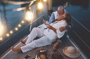 Senior couple kissing during sailboat vacation - Happy mature people having tender moments celebrating wedding anniversary on boat trip - Love relationship and travel lifestyle concept photo