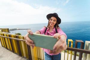 Young woman taking selfie with mobile smartphone during city excursion - Travel influencer having fun with social media in vacation - Millennial people and technology concept photo