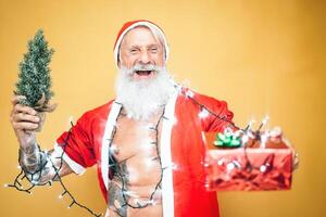 Happy tattoo hipster santa claus equiped with white lights giving christmas gifts - Trendy beard senior wearing xmas clothes and holding presents - Celebration and holidays concept photo
