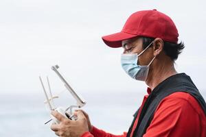 Man piloting drone while wearing face mask to avoid corona virus spreading - Technology and industrial concept photo