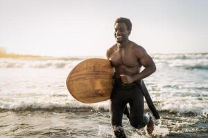 Male afro surfer having fun surfing during sunset time - African man enjoying surf day - Extreme sport lifestyle people concept photo