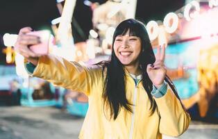 asiático niña tomando selfie con móvil teléfono en diversión parque - contento mujer teniendo divertido con nuevo tendencias teléfono inteligente aplicaciones - juventud milenario personas Generacion y social medios de comunicación adiccion concepto foto