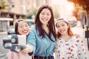 Happy Asian friends making video story in the city center - Trendy young people recording with gimbal smartphone  outdoor - Friendship, technology, youth lifestyle and social media concept photo