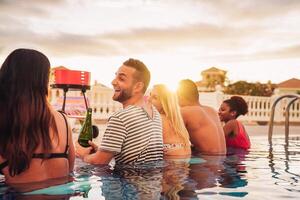 contento amigos haciendo un piscina fiesta Bebiendo champán en el junto a la piscina - joven personas en trajes de baño teniendo divertido a parilla cena en lujo tropical recurso a puesta de sol - juventud Días festivos estilo de vida concepto foto