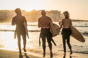 Happy fit surfers with different age and race having fun during surf day on the beach at sunset time - Extreme sport lifestyle and friendship concept photo