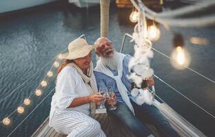 Senior couple toasting champagne while taking selfie on sailboat vacation - Happy mature people having fun celebrating wedding anniversary on boat trip - Love relationship and travel lifestyle concept photo