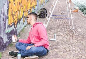 Street artist painting colorful graffiti on a wall under the bridge - Urban man performing with murales - Concept of modern contemporary art photo