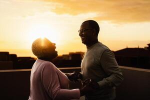 Happy Latin senior couple having romantic moment on rooftop during sunset time - Elderly people love concept photo