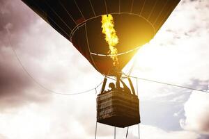 Hot air balloon flying in a cloudy sky at sunrise - Image of balloon silhouette flight over the sky photo