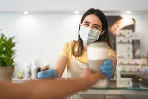 Bar owner working only with take away orders during corona virus outbreak - Young woman worker wearing face surgical mask giving coffee to customer - Healthcare and drinks concept photo