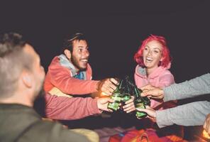 Happy friends toasting beers while camping outdoor - Group young people having fun making party together - Millennial generation and youth lifestyle culture holidays concept photo