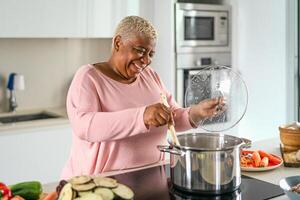 Happy senior woman preparing lunch in modern kitchen - Hispanic Mother cooking for the family at home photo